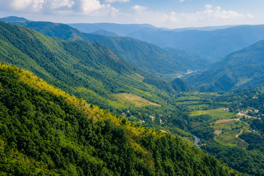 Lush green mountains with scattered villages in a wide valley under a partly cloudy sky, with distant blue mountain ranges fading into the horizon.