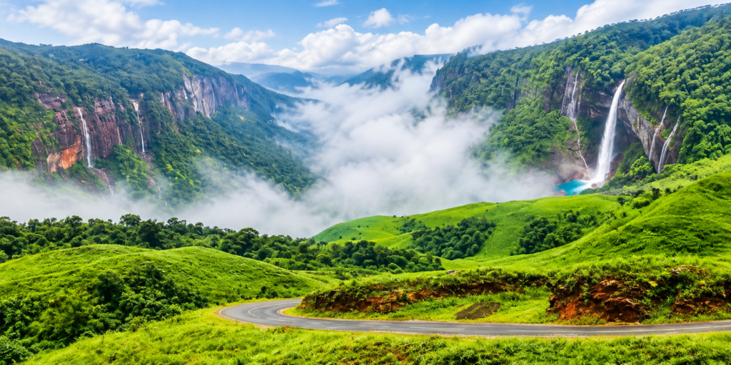 A winding road passes through lush green hills with a tall waterfall cascading into a blue pool, surrounded by mist and forested mountains under a partly cloudy sky.